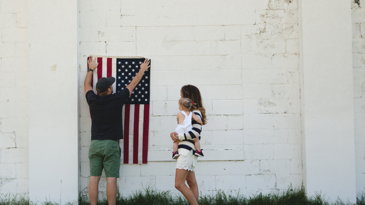 Expat women in the U.S. with baby as husband hangs American flag