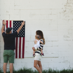 Expat women in the U.S. with baby as husband hangs American flag